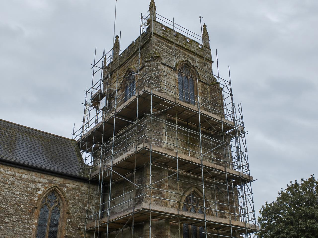 Scaffold surrounding a stone church tower with stained glass windows, boarded lifts to each stage