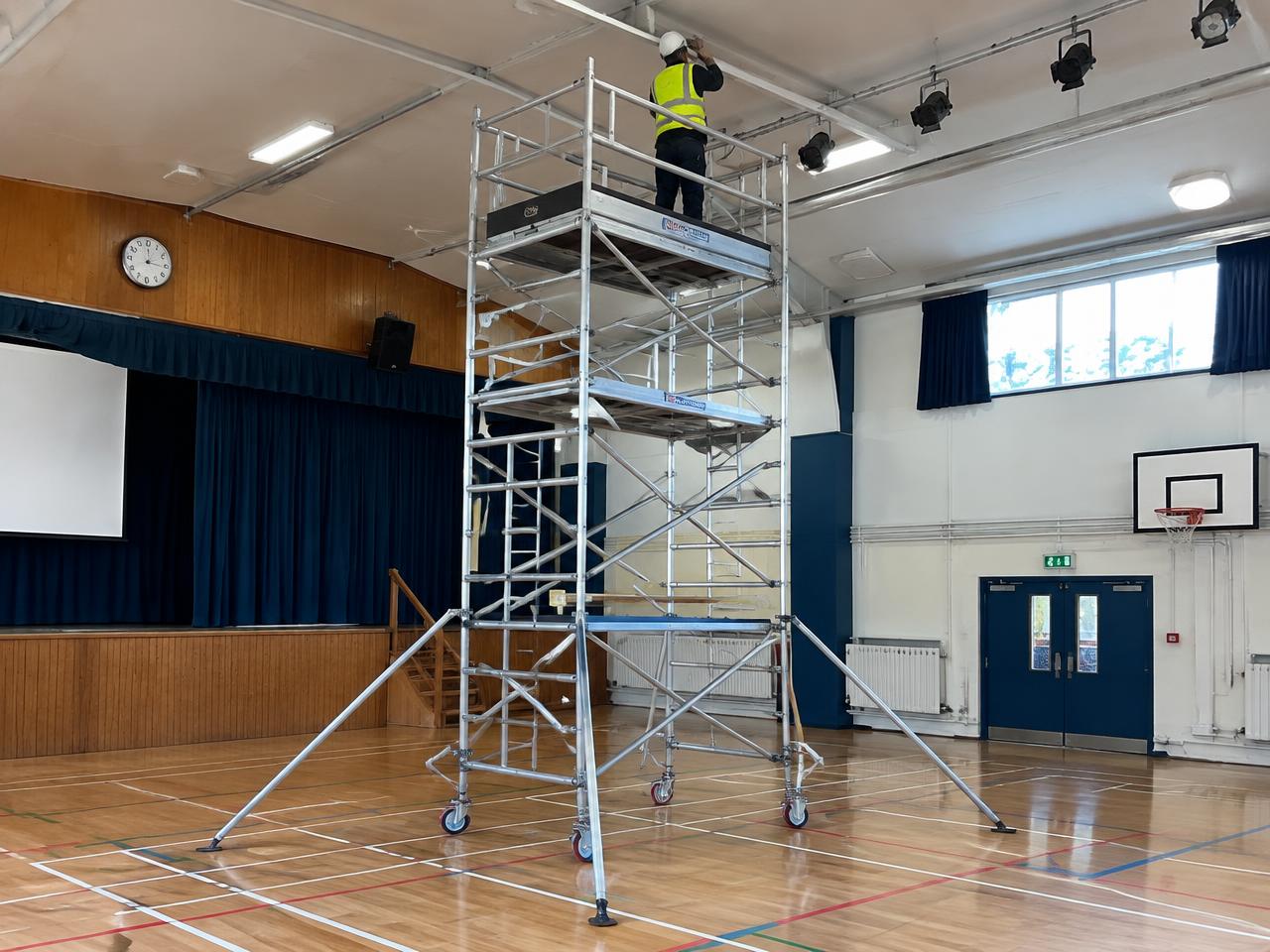 Aluminium mobile access tower erected inside a school hall for ceiling work, guard rails fitted