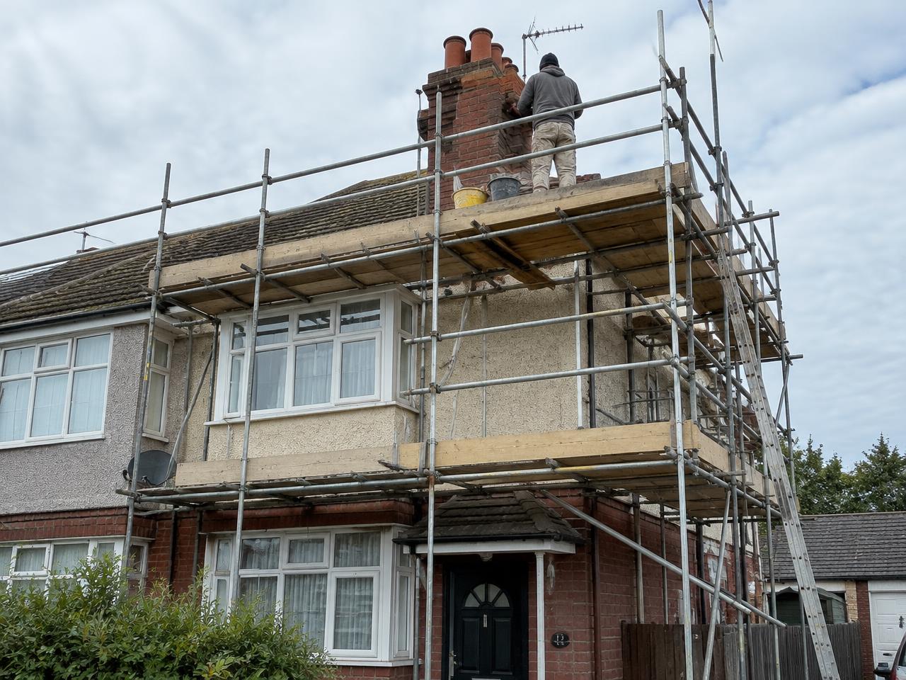 Two-lift scaffold around a semi-detached house with a scaffolder repointing the chimney stack