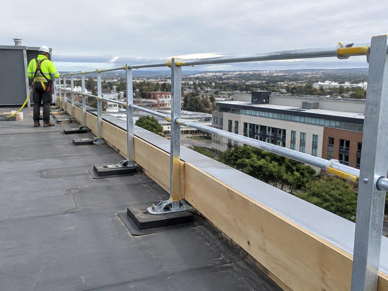 Galvanised edge protection handrail run along a flat roof perimeter with toe boards and a worker in a harness